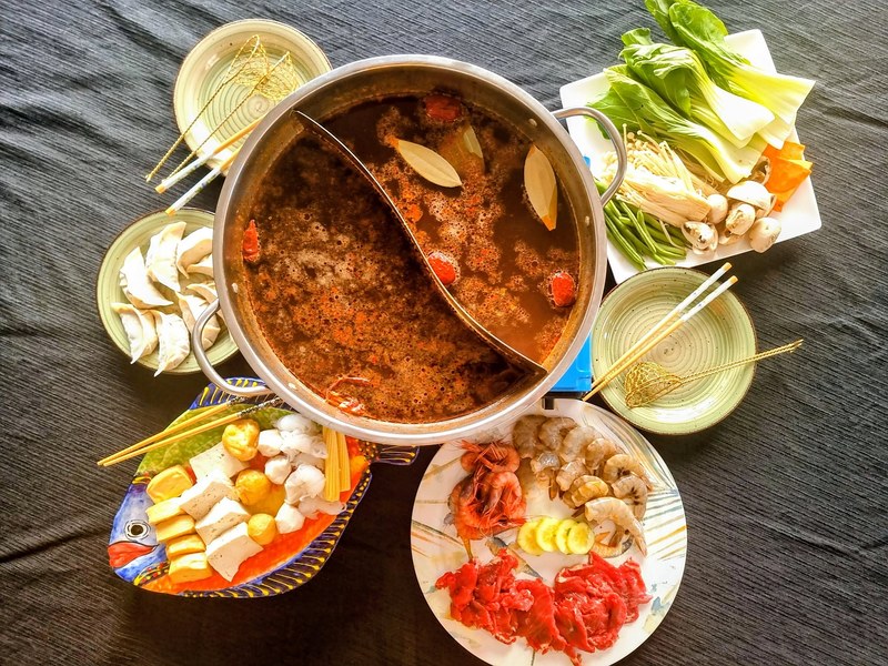 A divided hot pot ringed by plates of vegetables, meats, dumplings and skewers